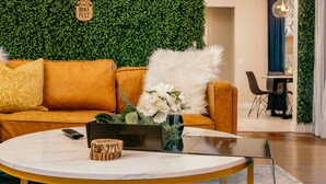 A modern living room with a green wall, a yellow sofa, a round coffee table, and a dining area in the background.
