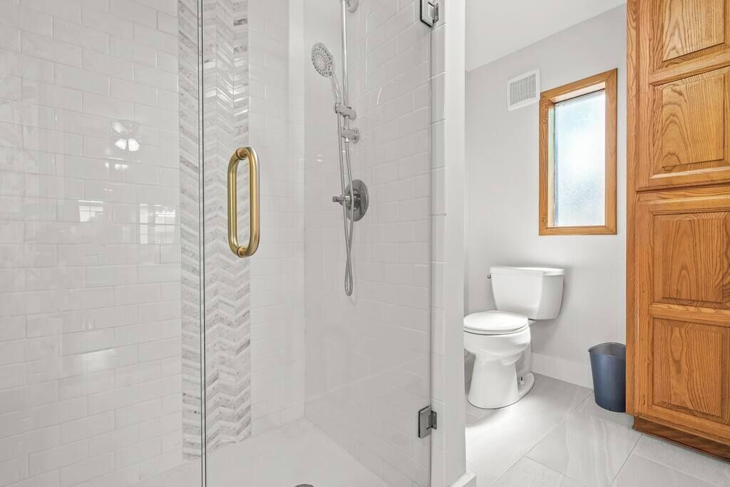 A bathroom with a glass shower enclosure, a toilet, and wooden cabinets.