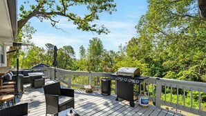 A wooden deck with outdoor furniture, a grill, and a trash can. - The Coves on Beaver Lake (Rogers)
