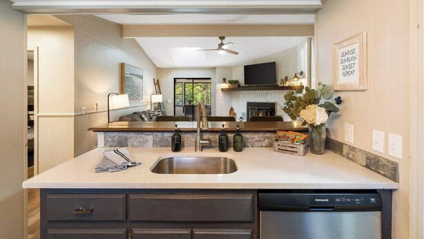 A modern kitchen with a stainless steel sink, dark cabinetry, and a built-in dishwasher. - The Coves on Beaver Lake (Rogers)