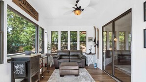 A spacious living room with a leather sofa, a coffee table, and a large window offering a view of the outdoors. There is a sign indicating boat rides and a wine sign on a cart. - The Coves on Beaver Lake (Rogers)
