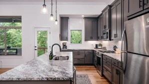 Une cuisine moderne dotée de plans de travail en granit, d’appareils électroménagers en acier inoxydable et de meubles de couleur sombre.