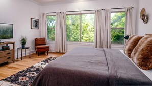 Une chambre avec un grand lit, une chaise, une télévision et une fenêtre avec des rideaux.