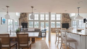 A spacious kitchen with a stone fireplace, large windows, and a dining area with wooden chairs and a table. - Stay at Smith Cove (Gloucester)