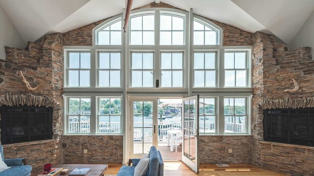 A spacious room with a high ceiling, stone walls, large windows, and a view of a dock. - Stay at Smith Cove (Gloucester)