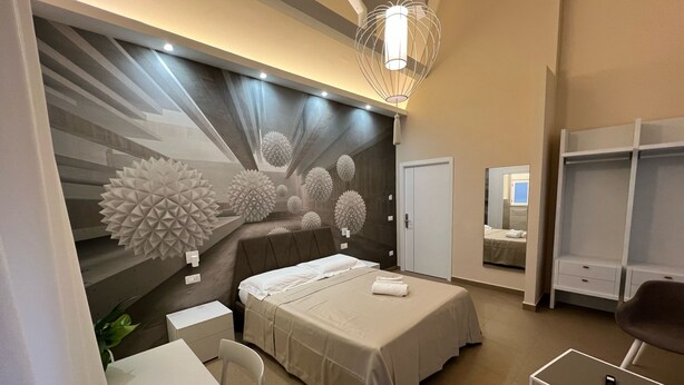 A modern bedroom with a bed, bedside table, chair, and a wall with geometric wall art. - Rupella  (Roccella Jonica)