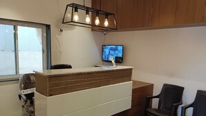 Un comptoir d’accueil avec un revêtement en bois, un téléviseur fixé au-dessus et deux chaises sur la droite.