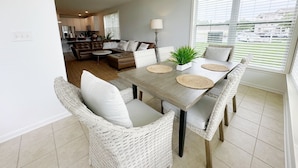 A dining area with a wooden table, white wicker chairs, and a potted plant. - Condo with Community Pool - 17432 Slipper Shell Way Unit 1 (Lewes)