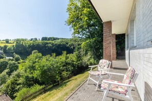 Een balkon met twee stoelen, een bakstenen muur en uitzicht op een groen landschap.