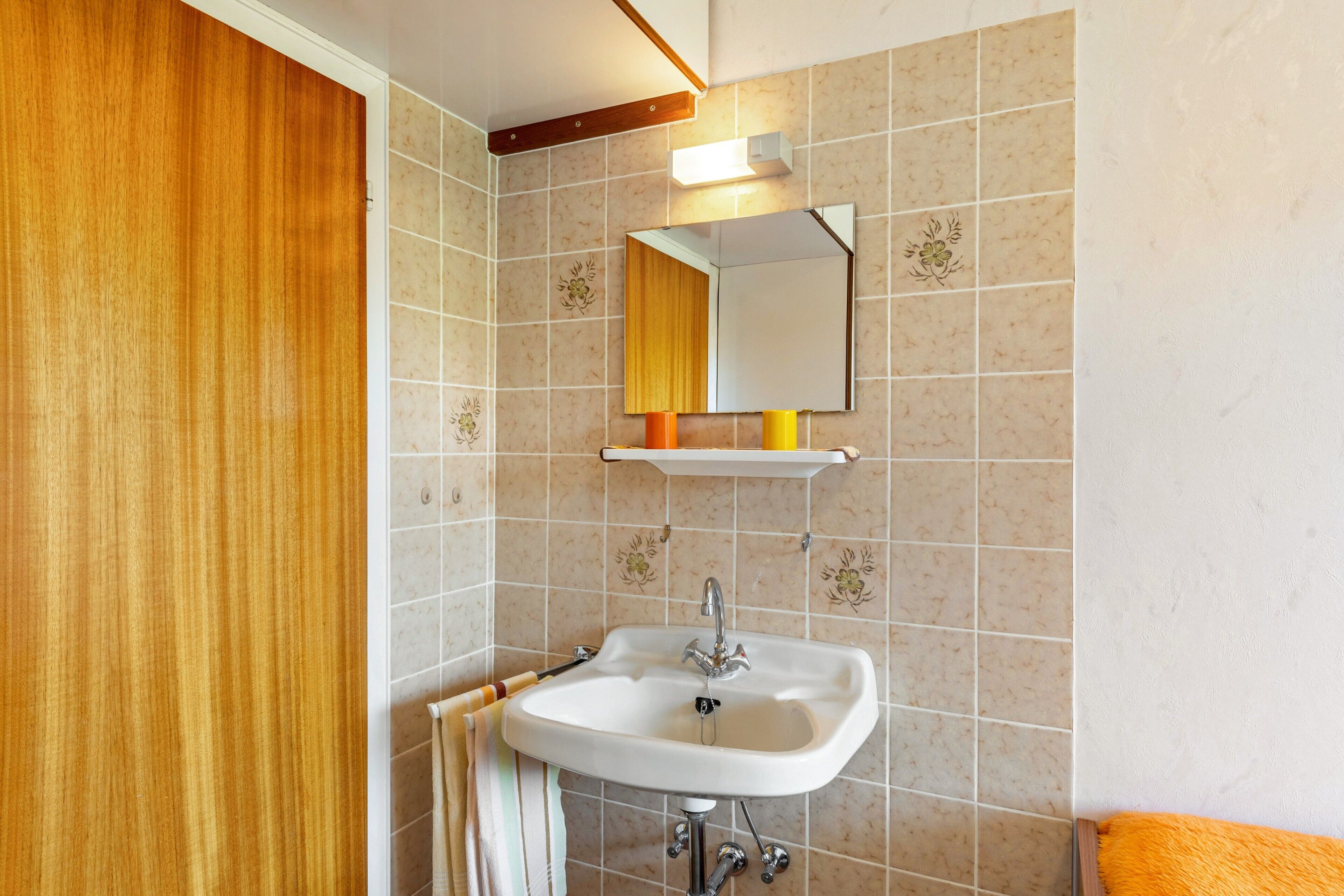 A bathroom with a wooden door, a white sink with a mirror above it, and a towel rack.