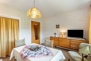 Een kamer met een tafel, stoelen, een televisie, een kast en een deur.