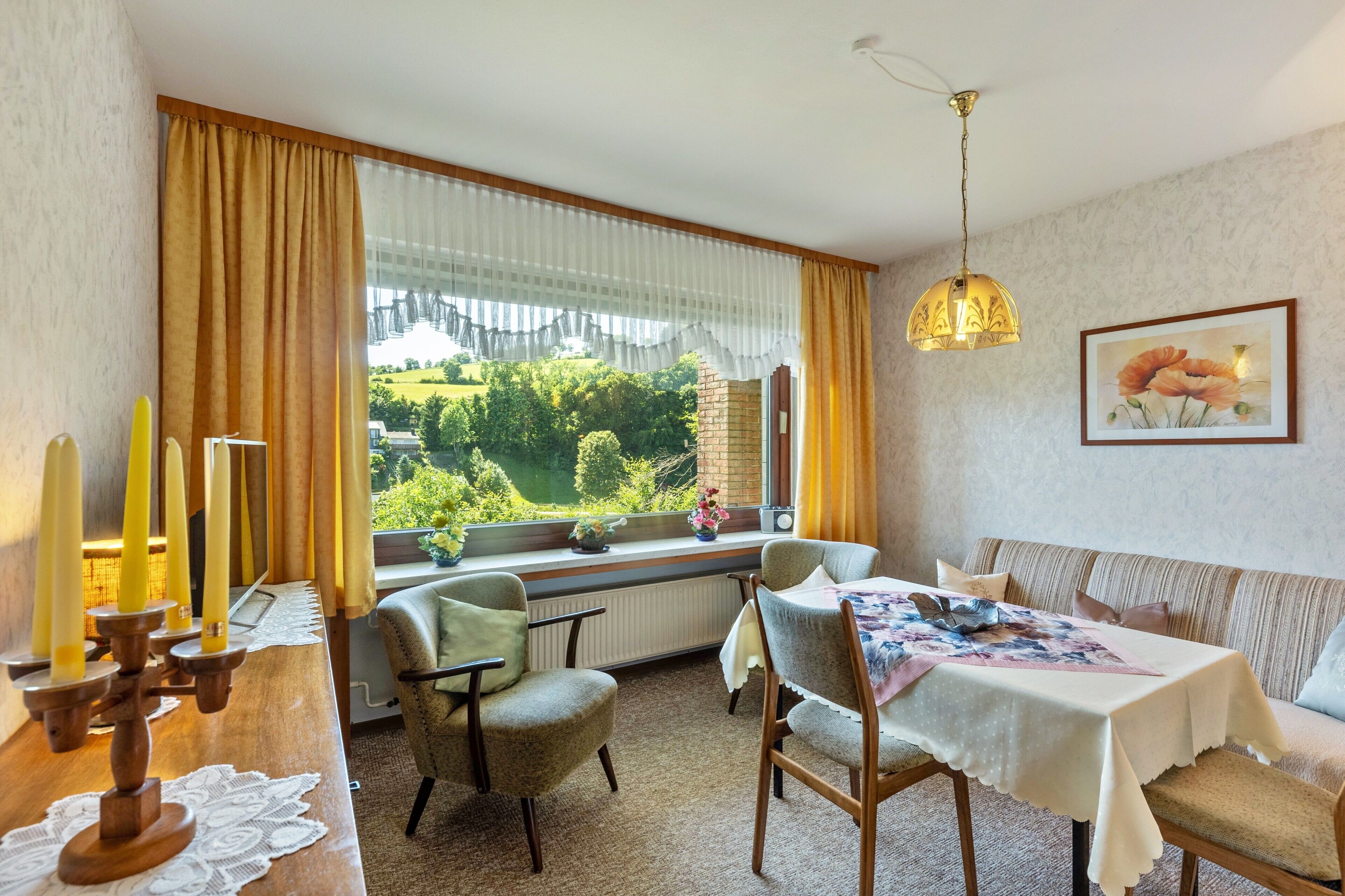 A dining area with a table, chairs, a window with curtains, a radiator, and a hanging light fixture.