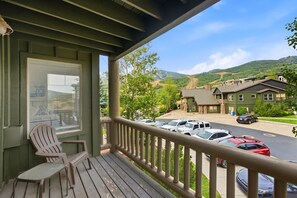 A wooden porch with a view of a parking lot and buildings in a hilly area.