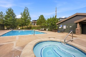 A swimming pool area with two pools, lounge chairs, and a building with pool rules posted.