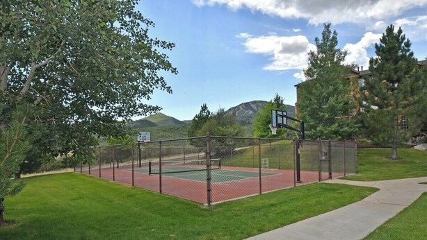 Una cancha de tenis rodeada por una cerca, con un aro de baloncesto y un cartel que indica el nombre de la cancha.