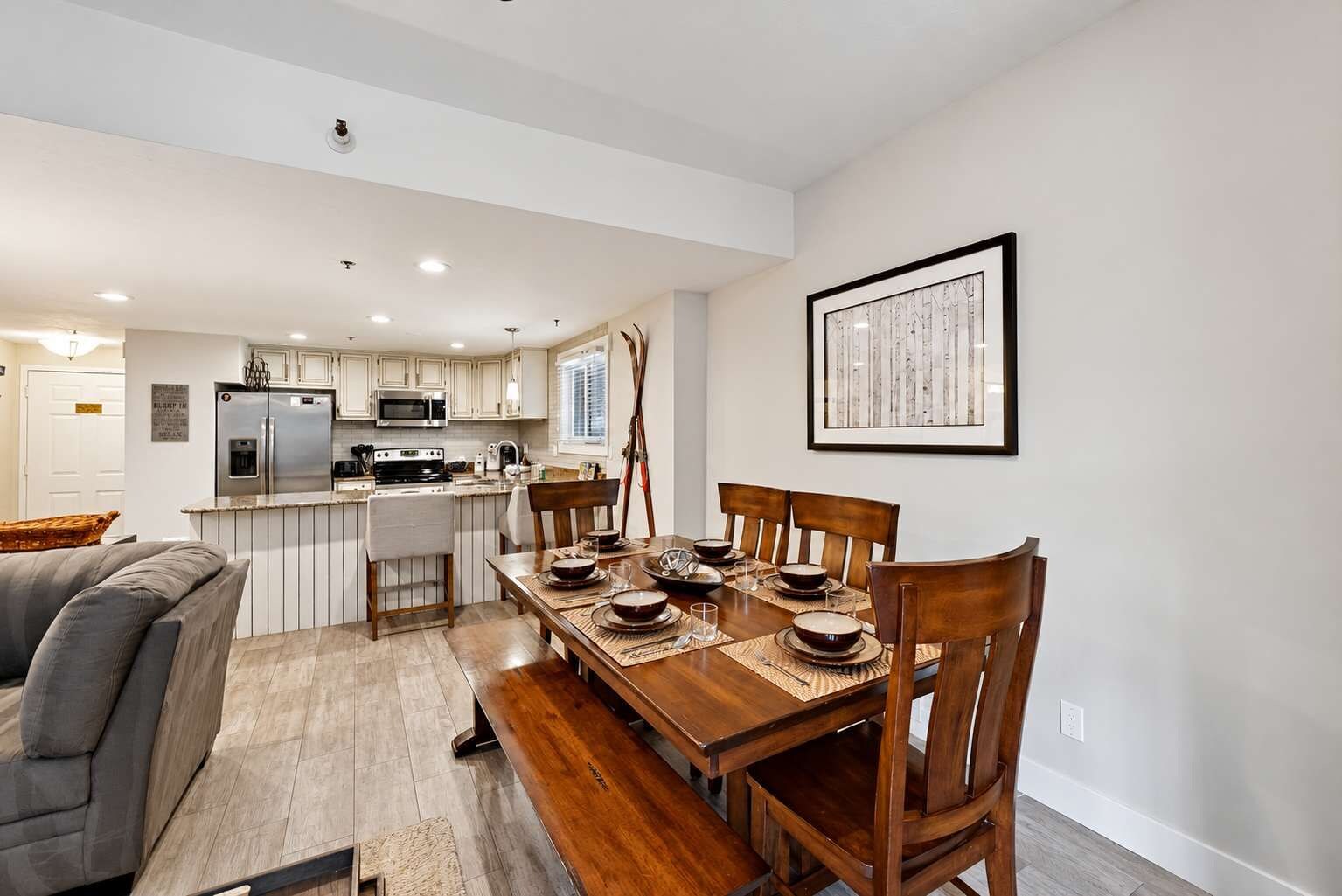 A modern kitchen with white cabinetry, a dining area with a wooden table and chairs, and a framed artwork on the wall.