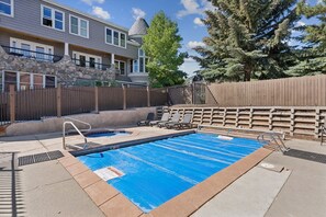 Una piscina con pared de piedra, valla de madera y vista a un edificio de varios pisos con torreón.