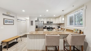 A modern kitchen with white cabinets, a granite countertop, stainless steel appliances, and a bar area with two stools. - Snowblaze Condo – Walk to Park City Mtn & Main St (Park City)