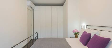 A bedroom with a bed, a nightstand, a vase with flowers, and a wall-mounted light.