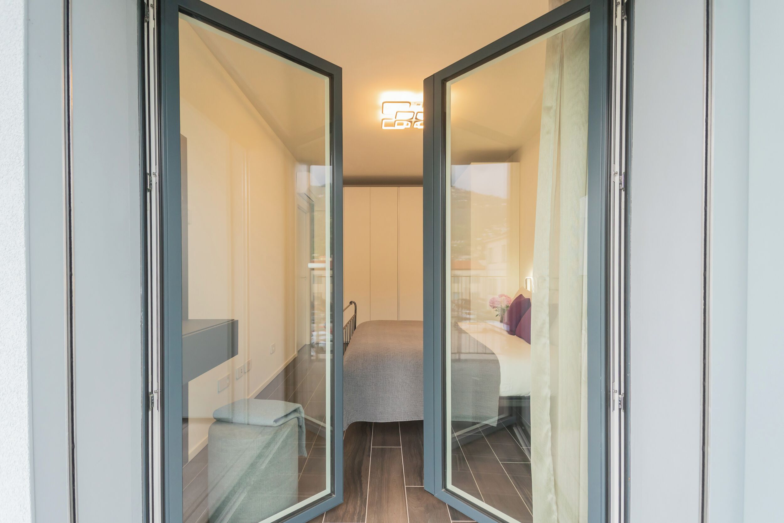 A modern hotel room with a glass door leading to a balcony, a bed, and a small seating area.