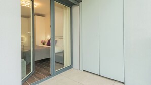 Una habitación moderna con una puerta de vidrio corredera que da a un baño, una cama con un almohadón y una mesita de noche con una lámpara.