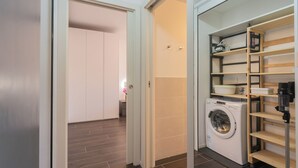 Un lavadero con lavadora, estanterías de madera y una puerta que da a otra habitación.