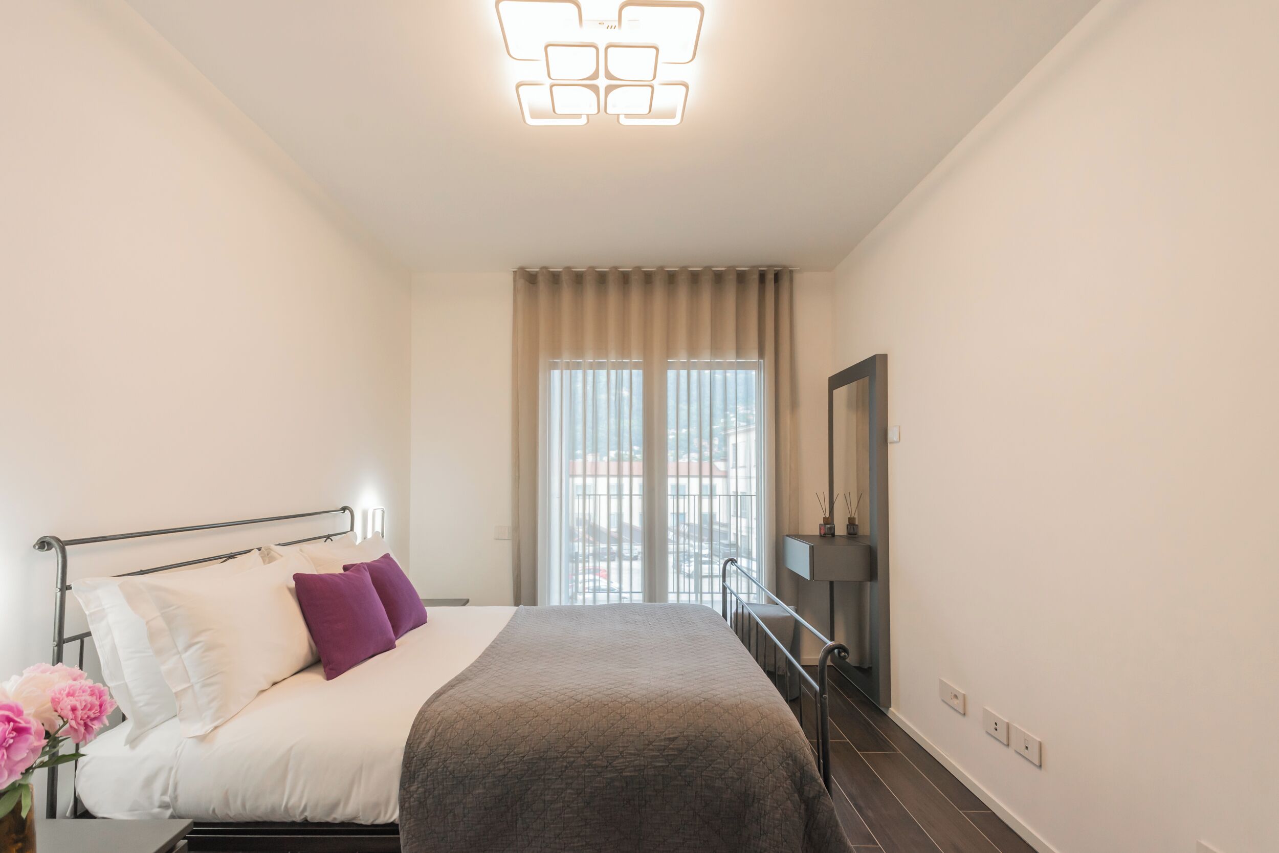 Una habitación de hotel moderna con cama, mesita de noche, espejo y ventana con cortinas.