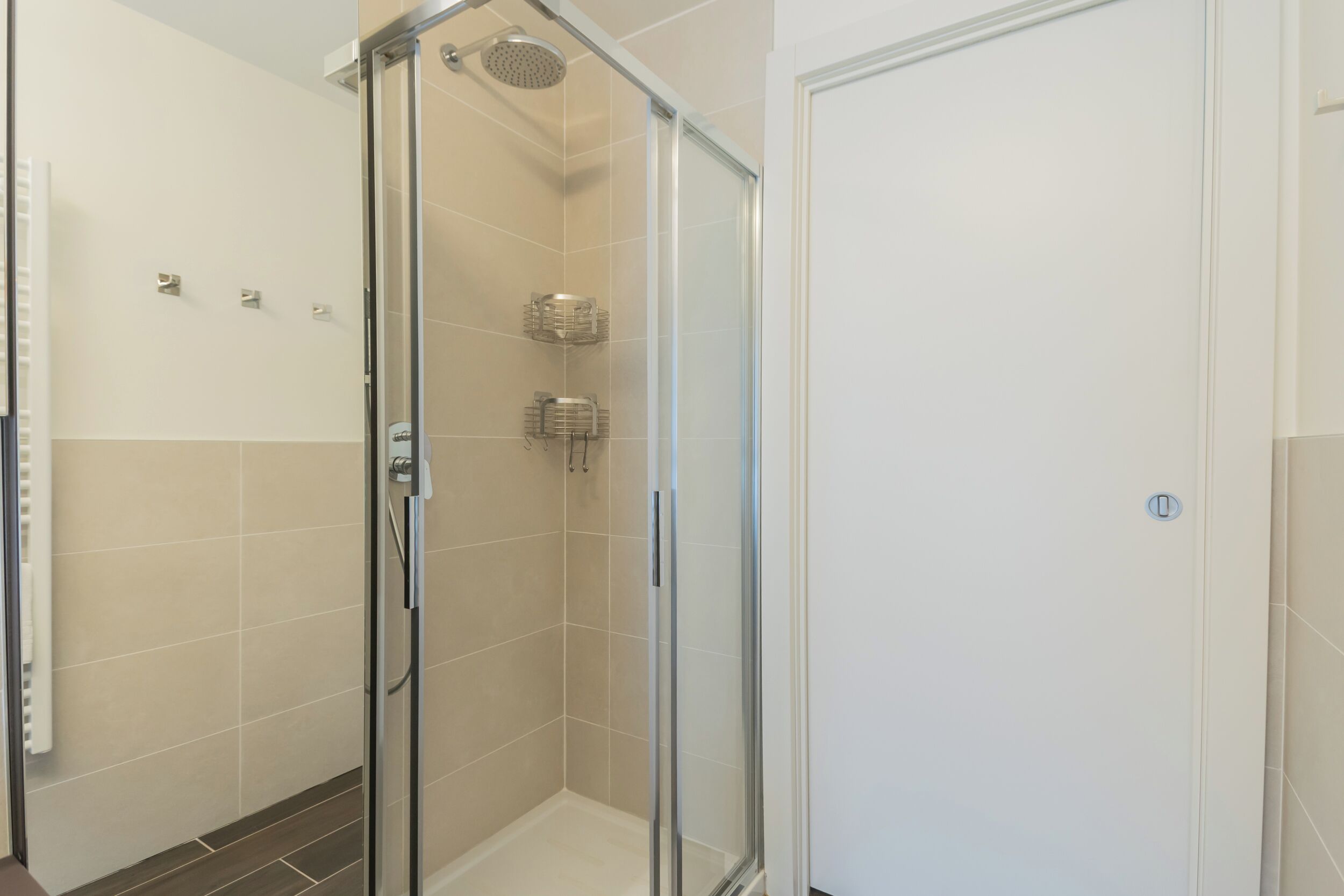 A glass-enclosed shower with a handheld showerhead, a towel rack, and a control panel.