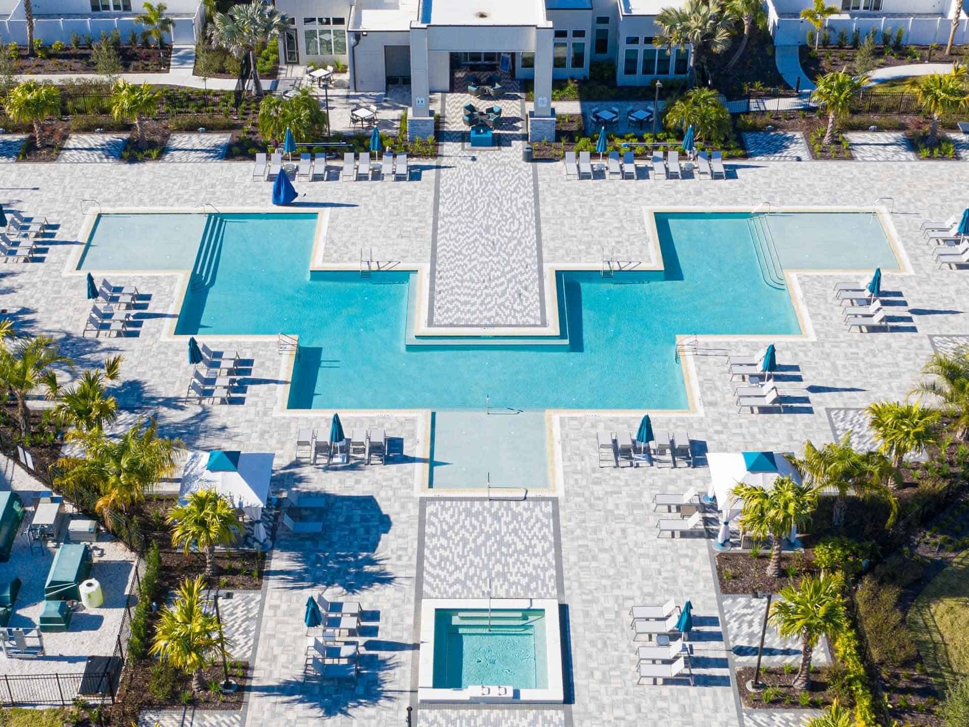An aerial view of a resort with multiple swimming pools, sun loungers, and palm trees.