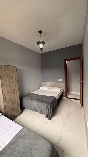 A bedroom with two beds, a wardrobe, a door, and a ceiling light. - Residencial Águia - Piske Imóveis (Florianopolis)