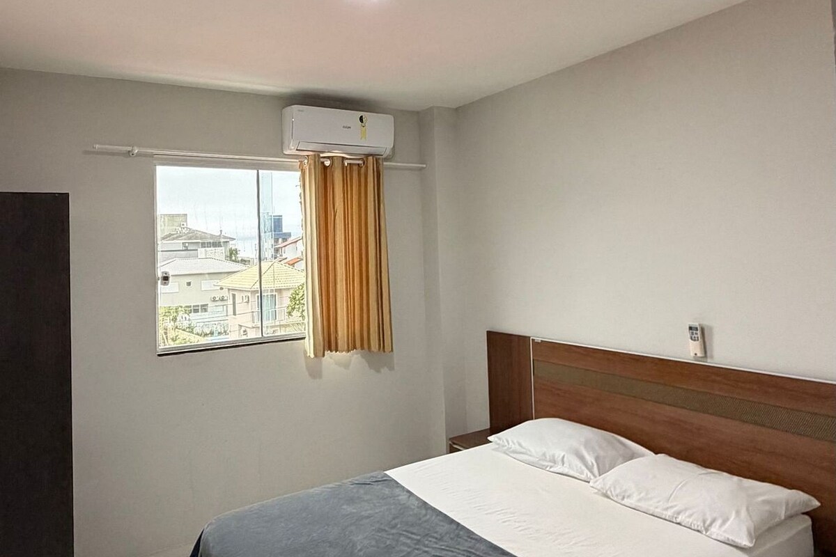 Una camera da letto con un letto, una finestra con tende, un condizionatore e un comodino.