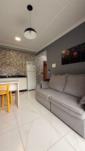 A modern kitchen with a white refrigerator, a dining table with yellow chairs, and a grey sofa.