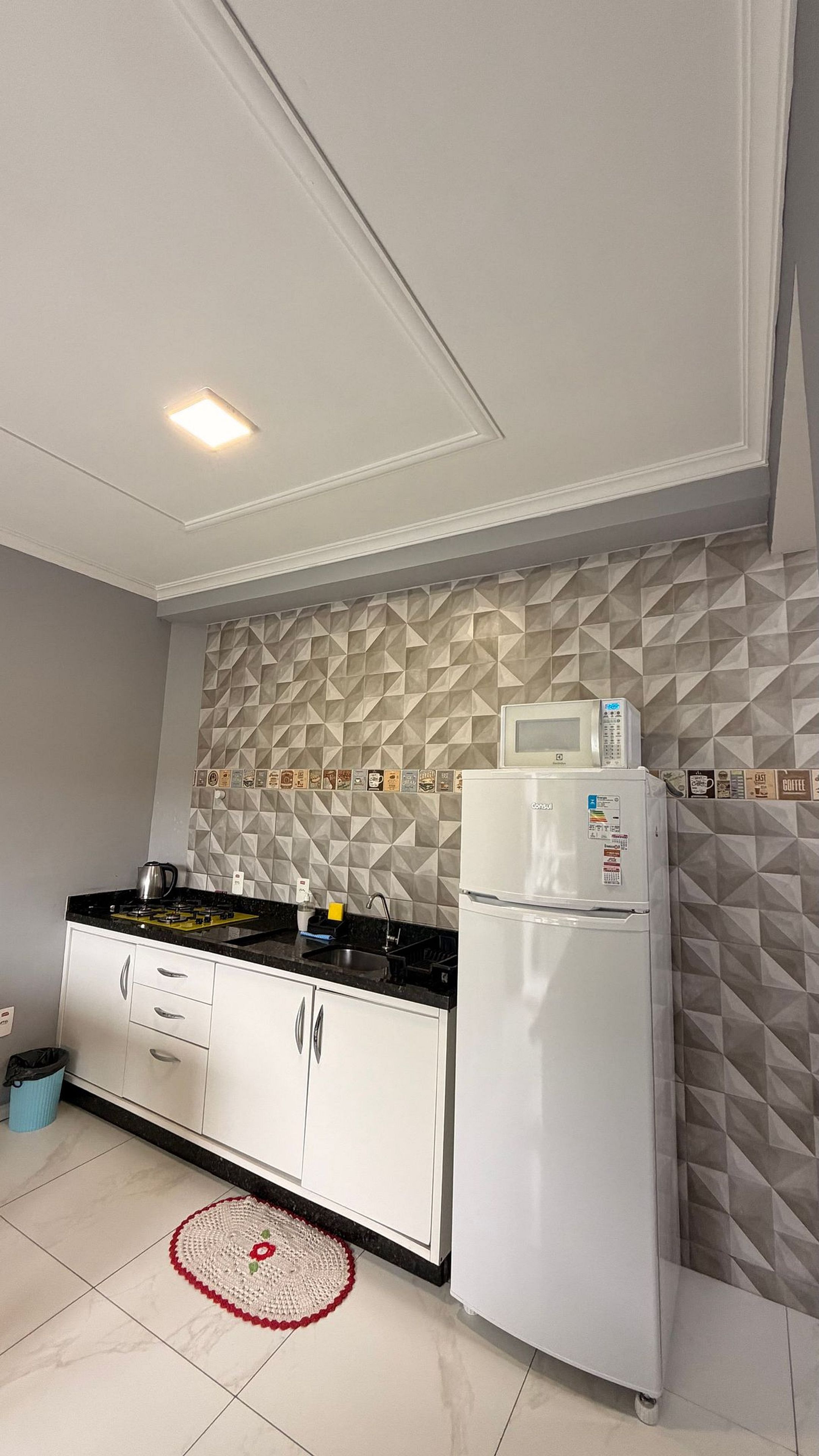 Une cuisine moderne avec des meubles blancs, un plan de travail noir, un four à micro-ondes et une machine à café.