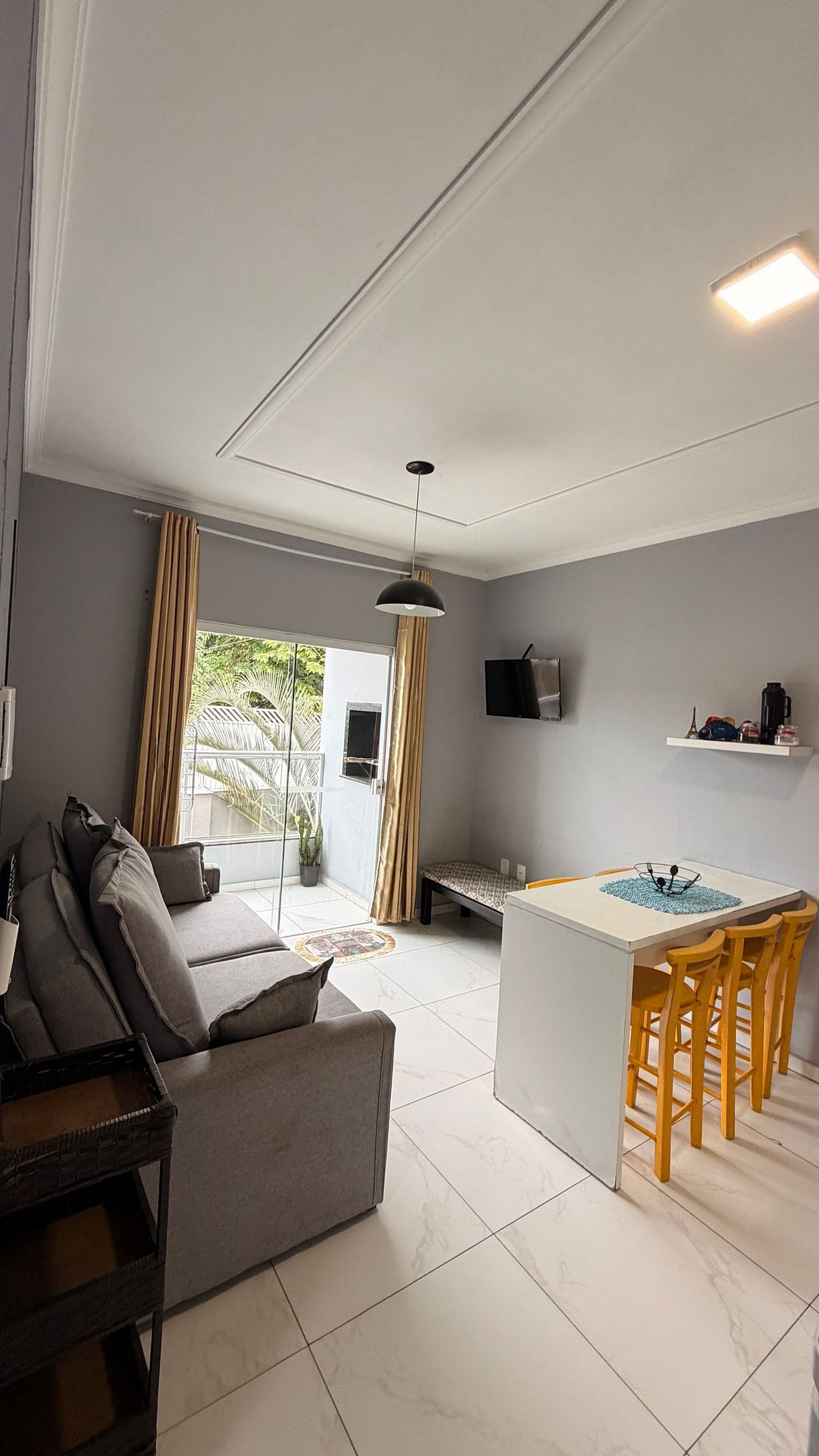 Un salon moderne avec un canapé, une table à manger et des chaises, un téléviseur fixé au mur et une fenêtre avec des rideaux.