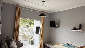 Un salon moderne avec un canapé, une table à manger et des chaises, un téléviseur fixé au mur et une fenêtre avec des rideaux.