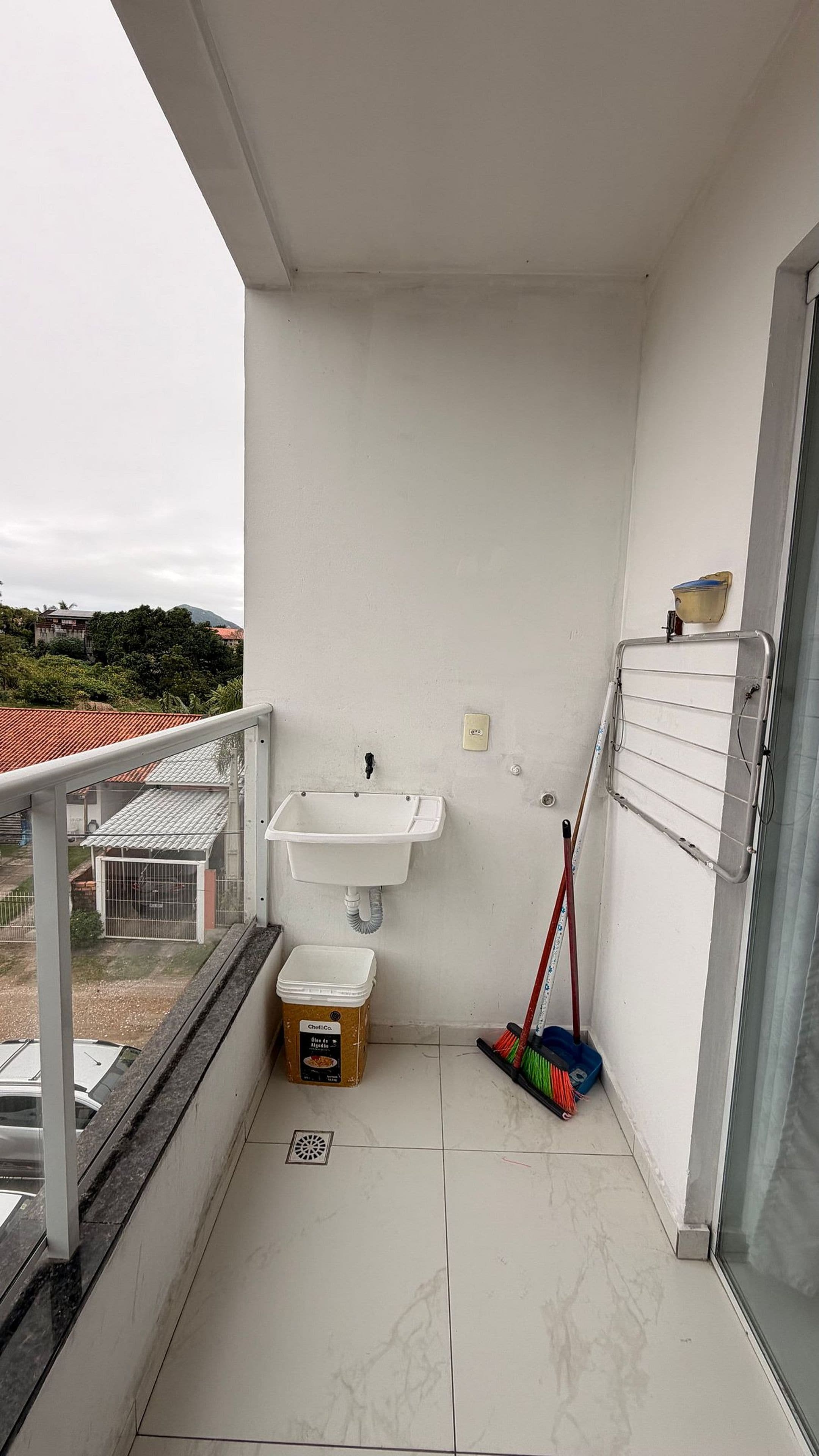 En lille balkon med en hvid vask, en kost og en spand.