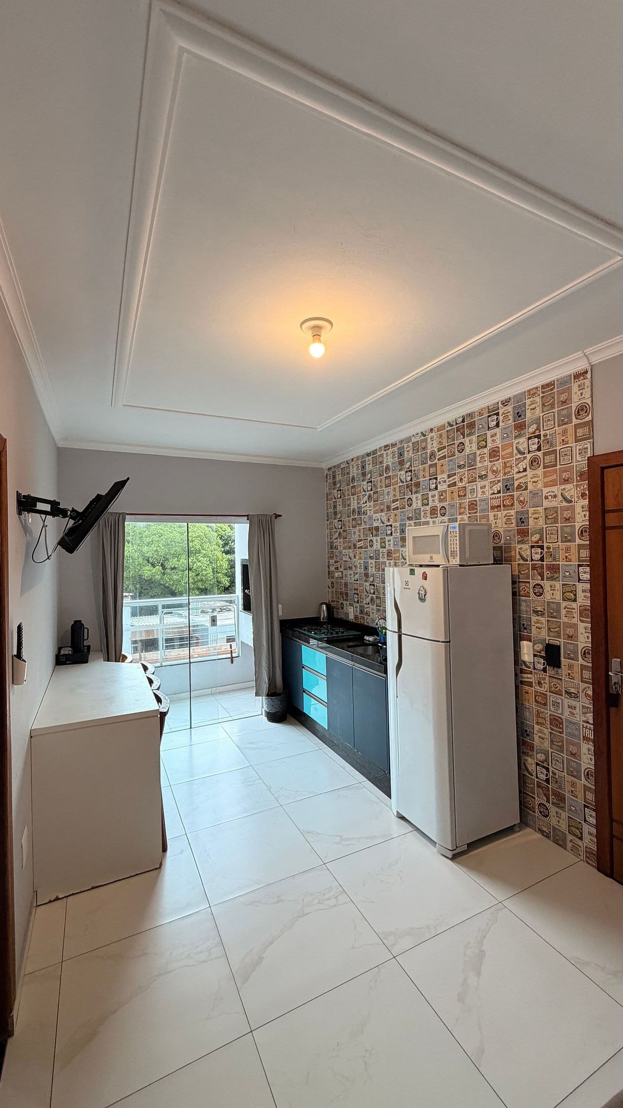 Una cocina con refrigerador, microondas y ventana con cortinas.