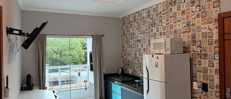 Una cocina con refrigerador, microondas y ventana con cortinas.