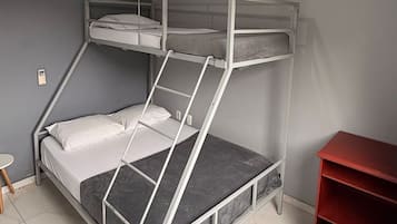 Uma cama beliche com escada, uma mesinha e uma estante vermelha num quarto com paredes cinzentas e teto branco.