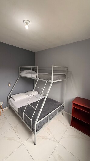 A bunk bed with a ladder, a small table, and a red shelf unit in a room with grey walls and a white ceiling.