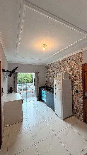 A kitchen with a refrigerator, microwave, and a window with curtains. - Residencial Águia - Piske Imóveis (Florianopolis)