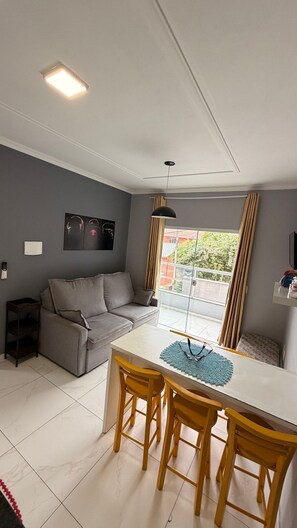 Una sala de estar moderna con un sofá gris, una mesa de comedor blanca con sillas amarillas, una lámpara de techo y vistas a un balcón.