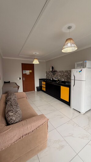 A modern kitchen with a refrigerator, microwave, and stove, a sofa with a patterned throw, and two pendant lights. - Residencial Águia - Piske Imóveis (Florianopolis)