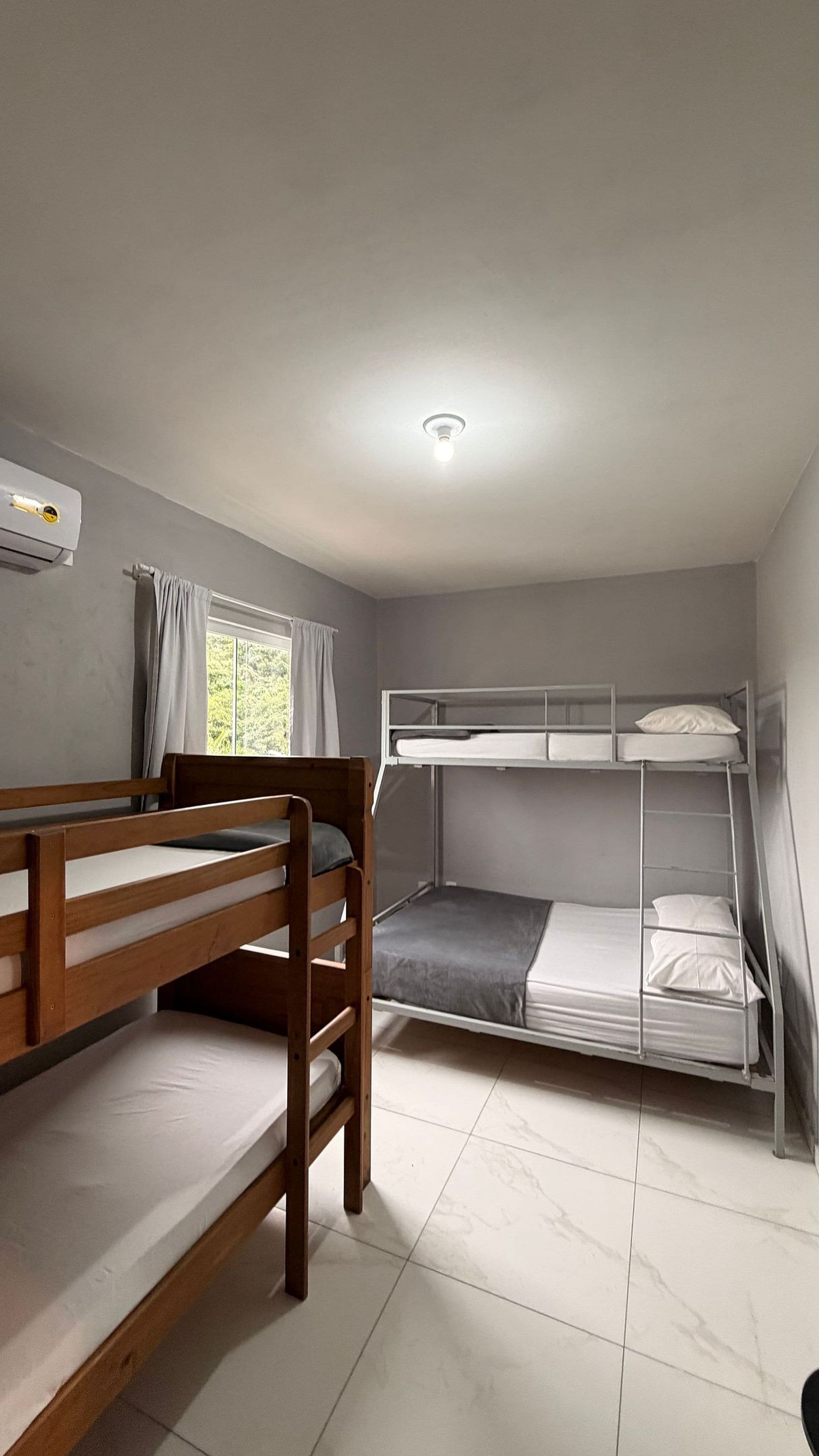 A dormitory room with bunk beds, a window with curtains, and a ceiling light.