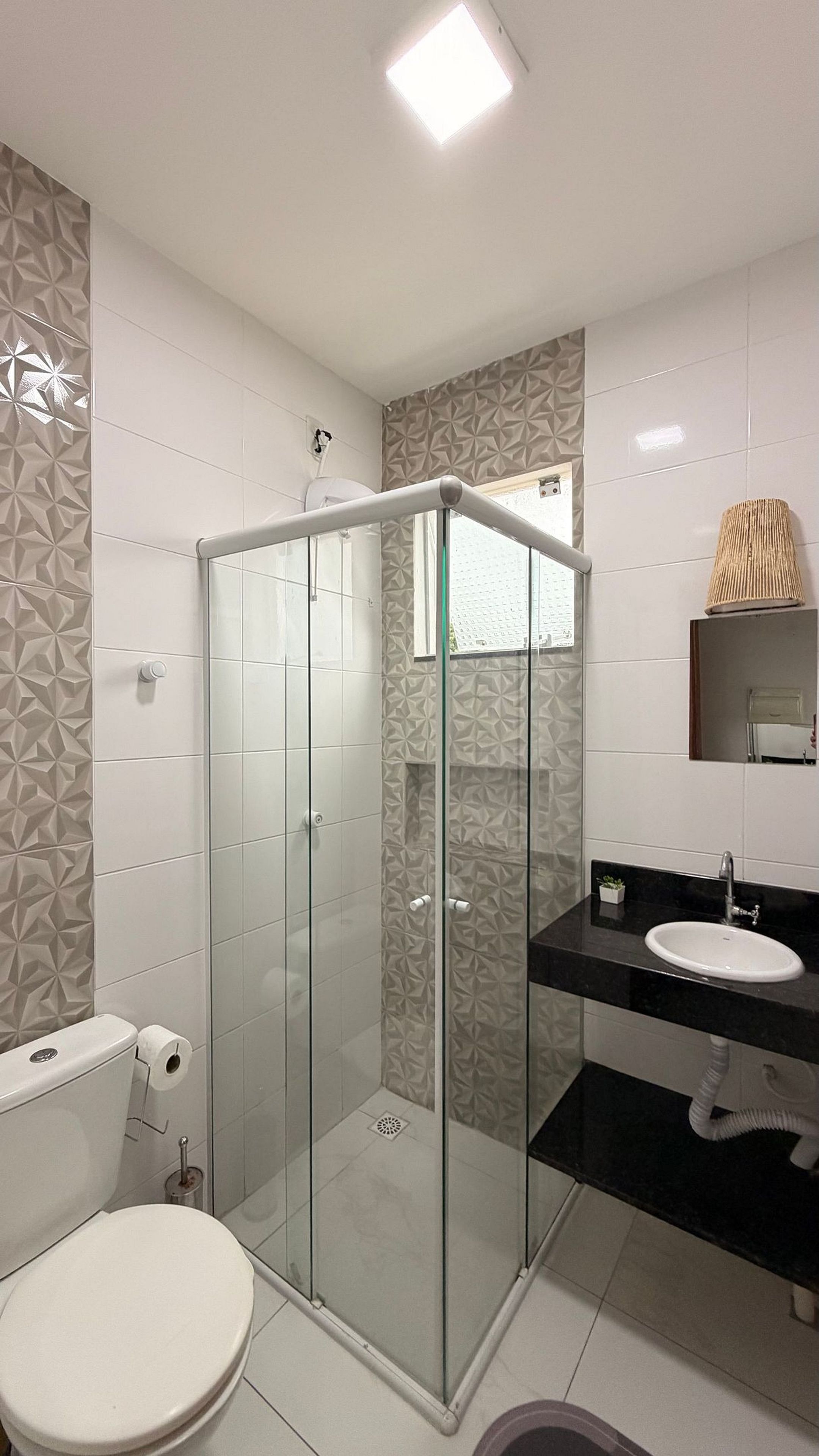 Un baño moderno con ducha de vidrio, inodoro, lavabo y espejo.