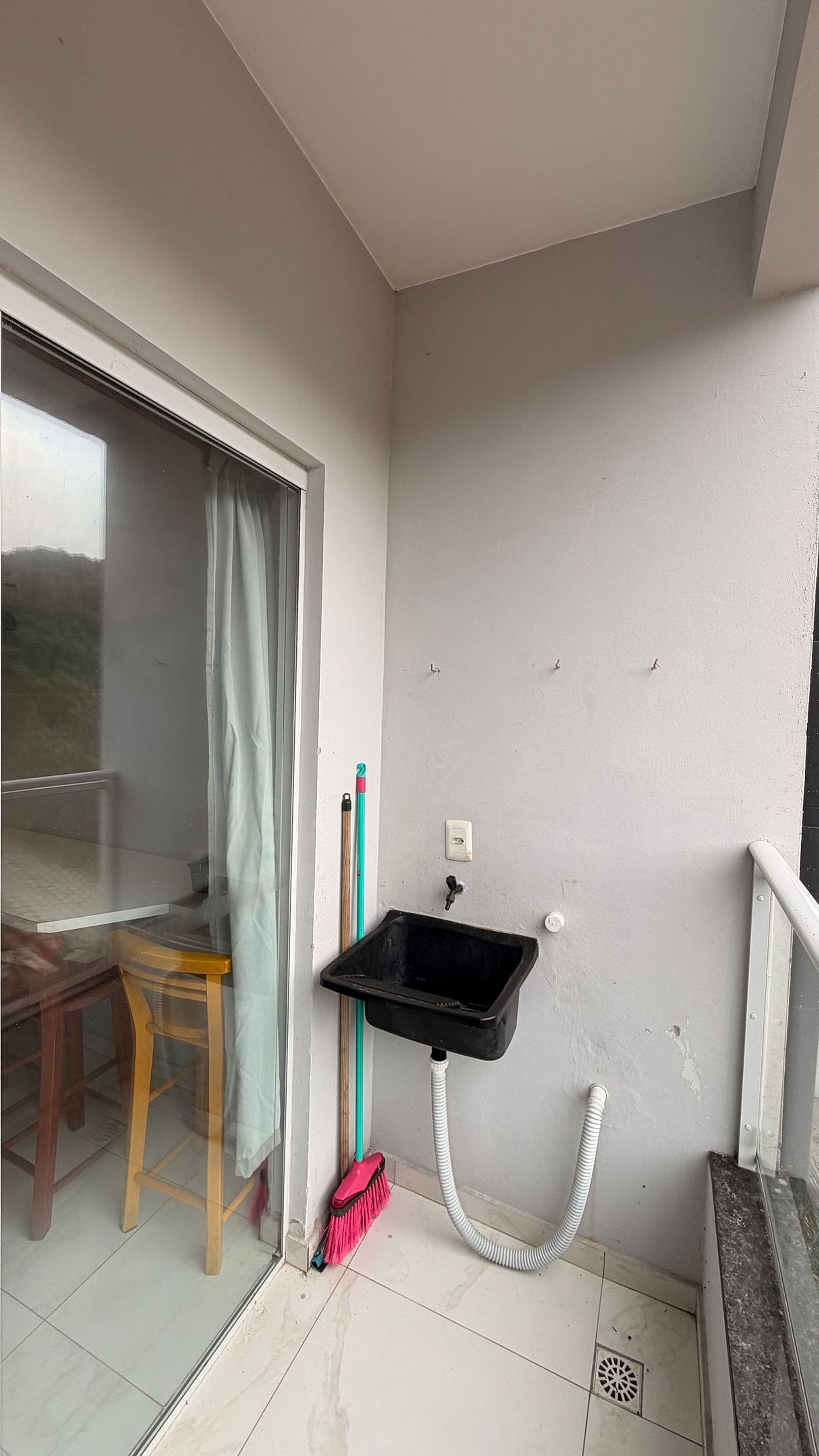 A small bathroom with a sink, a broom, and a chair.
