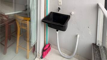 A small bathroom with a sink, a broom, and a chair.