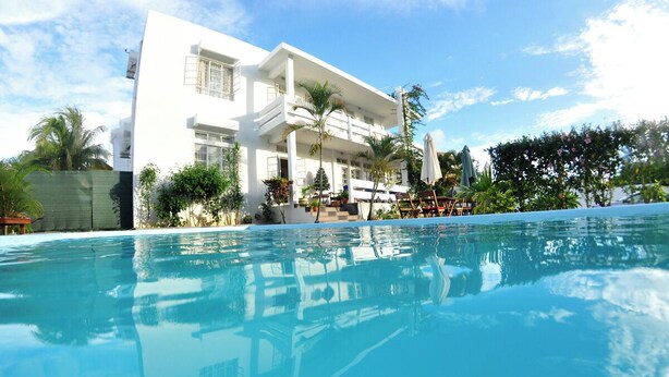 A modern hotel with a large pool, outdoor seating, and lush greenery. - Villa Osumare (Flic-en-Flac)