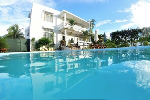 A modern hotel with a large pool, outdoor seating, and lush greenery.