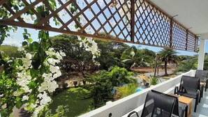 A balcony with a view of a pool and lush greenery, including white flowering plants. - Villa Osumare (Flic-en-Flac)